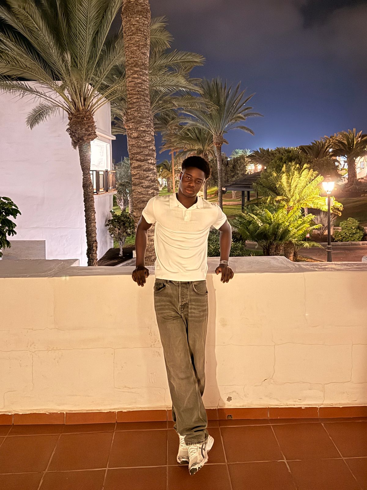 Taiwo standing outdoors at night, leaning against a wall